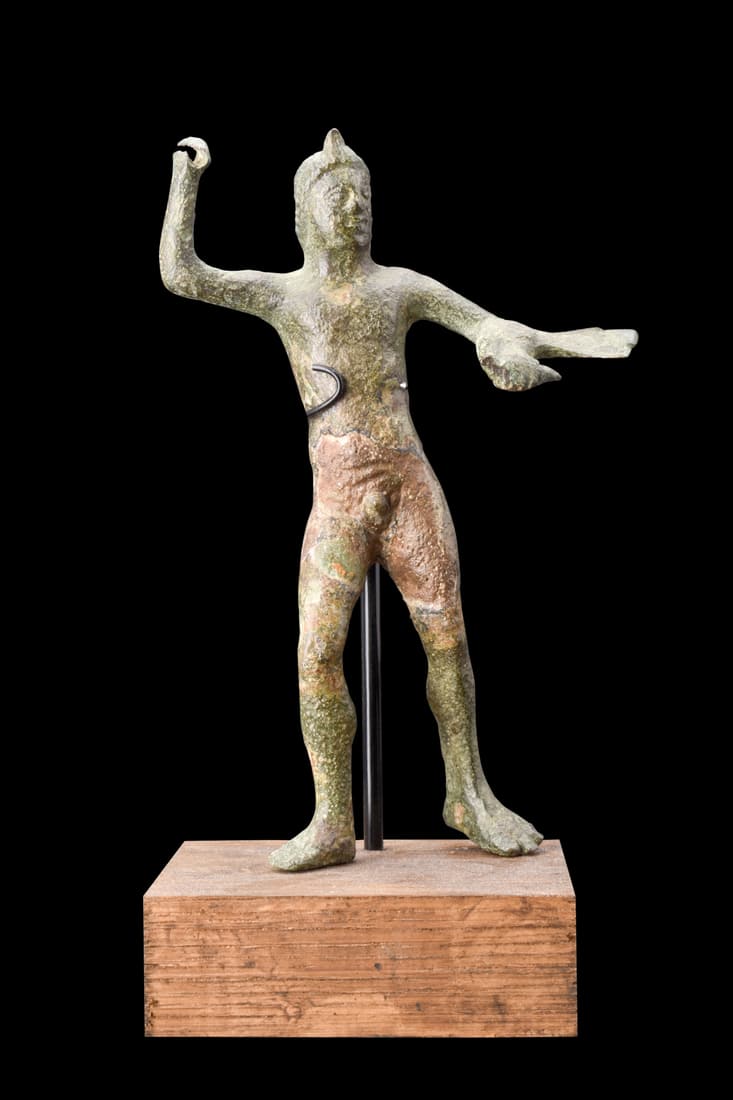 ETRUSCAN BRONZE STATUETTE OF HERAKLES: Ca. 300-200 BC.A bronze figurine of Herakles, depicted in a commanding standing pose. The statue features a subtle sway to his right, with his right leg slightly bent, and his right hand raised. His l
