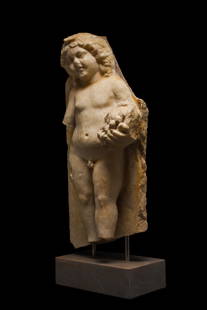 LARGE ROMAN MARBLE FIGURE OF CUPID HOLDING GRAPES- EX R.SORGE COLLECTION: Ca. 200 AD. A finely carved in extremely high relief – virtually in the round – section of a marble sarcophagus depicting the god Eros (Roman Cupid) or one of the Erotes (Roman Cupids)