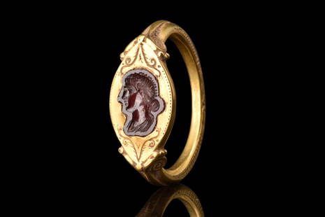 RARE ROMAN GOLD RING WITH GARNET INTAGLIO WITH FAUSTINA JUNIOR: Ca. late 2nd century AD. A gold ring with a D-shaped design, characterized by a round-section shank that expands at the shoulders and culminates in scroll finials. These finials elegantly support an