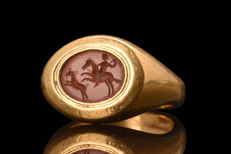 RARE ROMAN GOLD RING WITH CARNELIAN INTAGLIO DEPICTING A HUNTING SCENE - HEAVY GOLD: Ca. 100-300 AD. A rare gold, heavy signet ring composed of a round, flat-section hoop with expanded and carinated shoulders; bezel containing a carnelian intaglio depicting a hunting scene of a