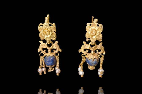 HELLENISTIC GOLD PAIR OF FILIGREE EARRINGS WITH DOLPHINS: Ca. 4th century BC. A breathtaking example of the intricate artistry and mastery of ancient goldsmiths. Each earring boasts a hook adorned with a stunning flower-shaped plaque, expertly crafted with