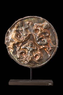 HELLENISTIC NEREIDS SILVER APPLIQUE ORNAMENT: Ca. 350 BC. Sheet silver applique ornament decorated in high relief with three nereids, bare-breasted mermaids, one holding a horn, one holding both hands to the sides of her head and one holding an