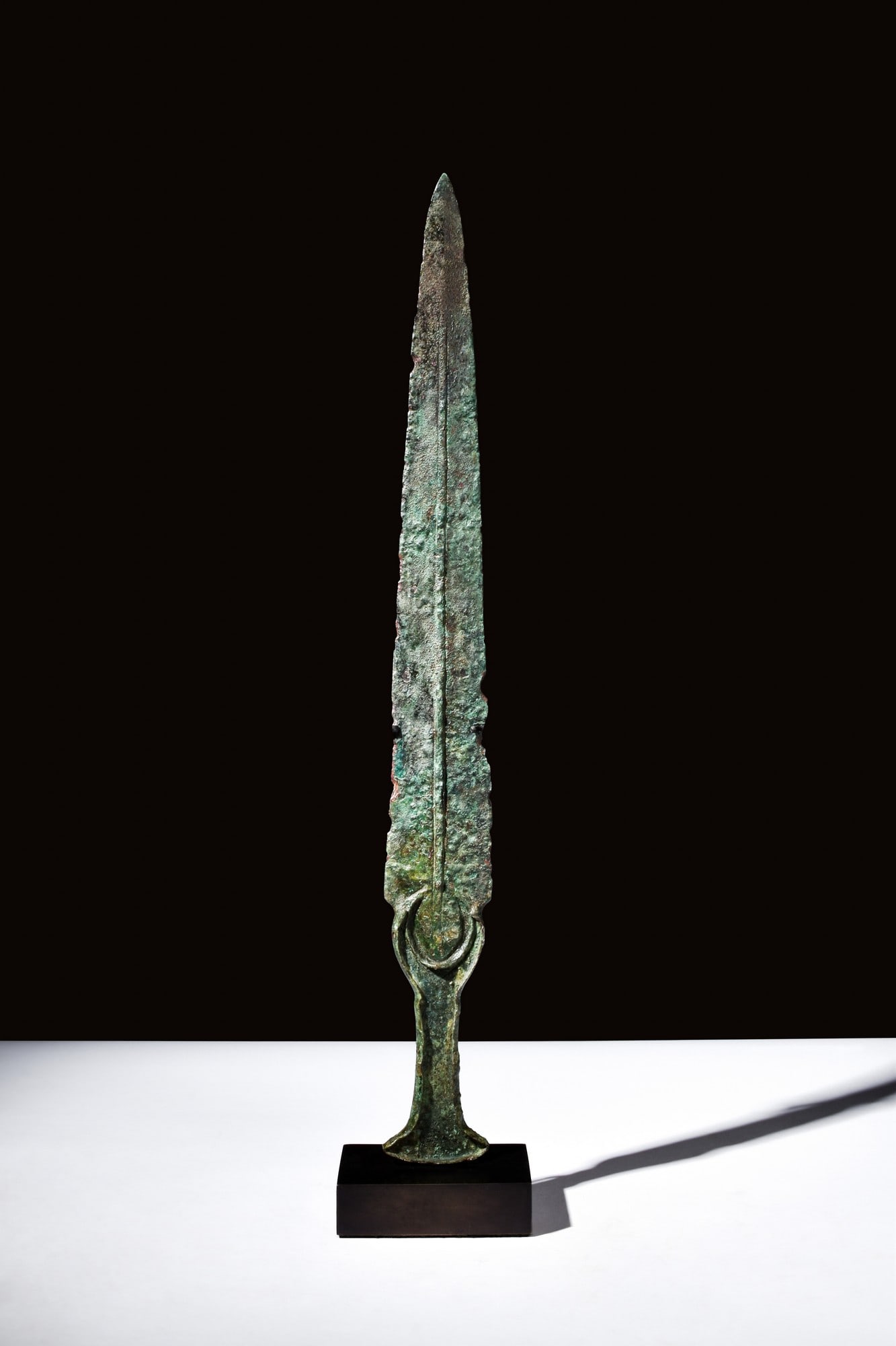 ANCIENT BRONZE SWORD: Western Asiatic/Aegan, ca. 1200-700 BC.A bronze sword with a sharp, tapered blade and a curved hilt. The pommel flares out, and the blade has a raised midrib. For similar see: The Metropolitan Museum