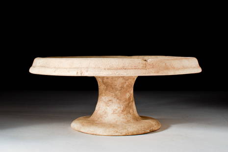 EGYPTIAN ALABASTER OFFERING TABLE: Ca. 2465-2150 BC.An alabaster offering table composed of a broad circular top with a thick, raised rim with a sloping side. It sits on a central cylindrical stem flaring to the disk foot. These