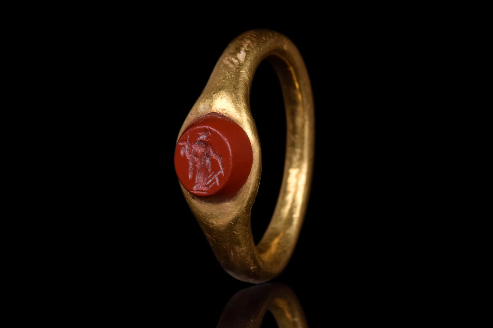 ROMAN GOLD RING AND CARNELIAN INTAGLIO DEPICTING FORTUNA: Ca. AD 200-300.An oval gold ring with jasper hardstone engraved with a standing profile figure of Fortuna, her head facing right, she is holding a rudder and cornucopia. Size: D:15.29mm / US: 4 1/4 /
