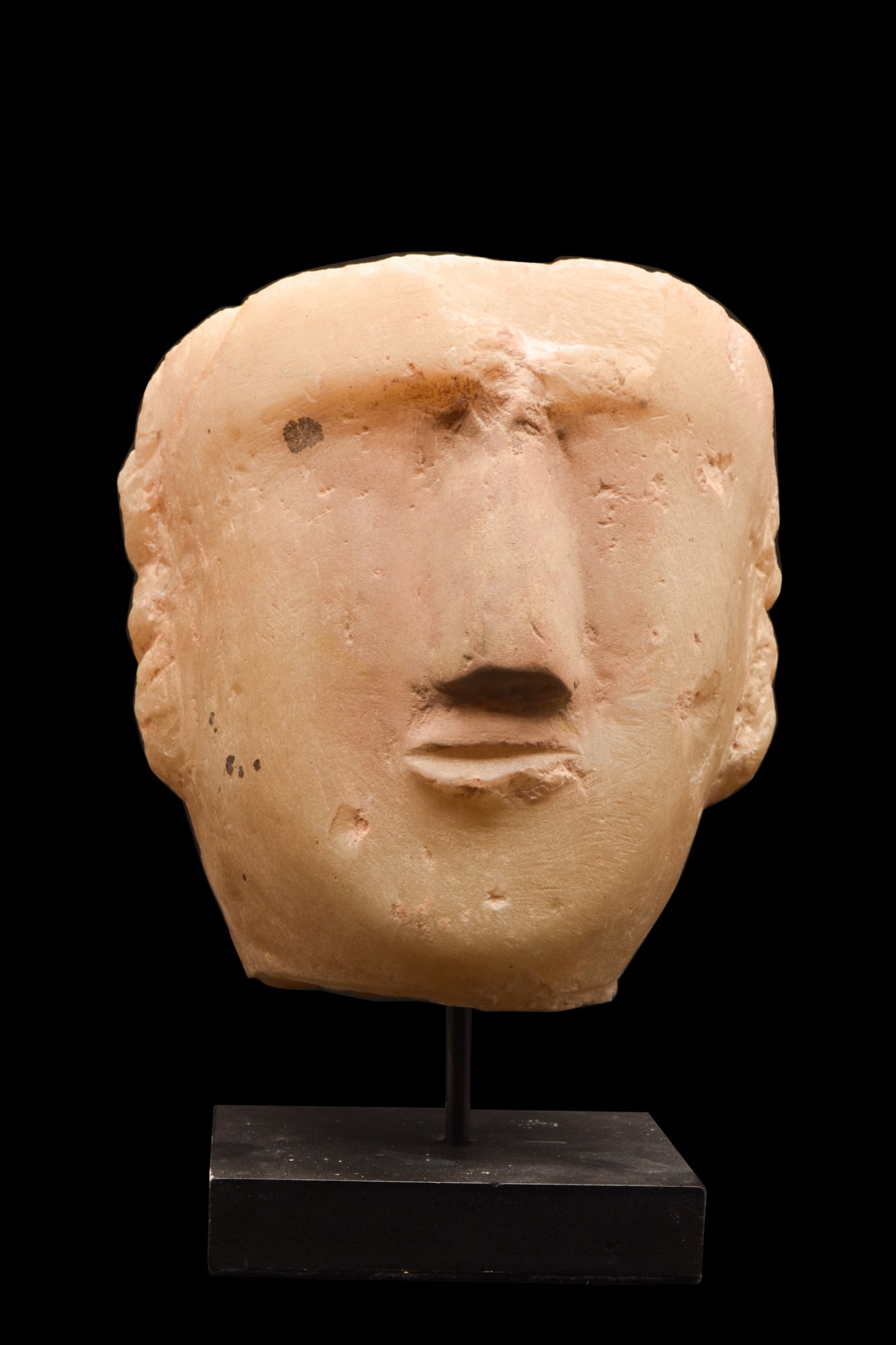 SOUTH ARABIAN ALABASTER FACE STELE: Ca. 200 BC - 100 AD.A hand-carved alabaster head of a man delineated in high relief, perhaps from a funerary stele, presenting a quixotic visage comprised of gazing, wide-open eyes, an arched browline