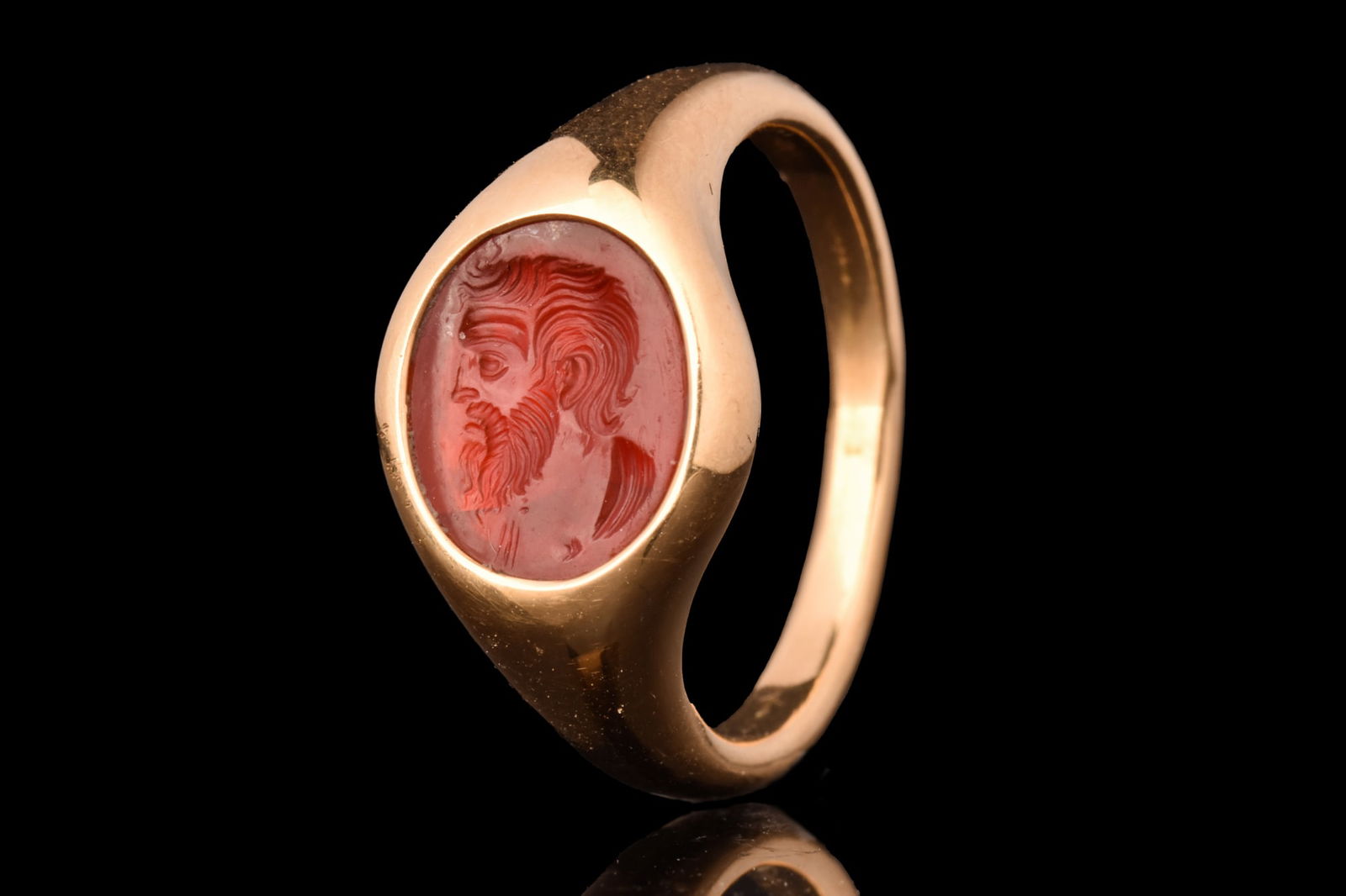 HELLENISTIC INTAGLIO OF BEARDED MALE PORTRAIT IN GOLD RING: Ca. 400 BC.A carnelian stone intaglio finely engraved with a left-facing portrait of a mature male. His countenance with wide-open eyes, prominent nose, wrinkled forehead, abundant beard and nonchalan