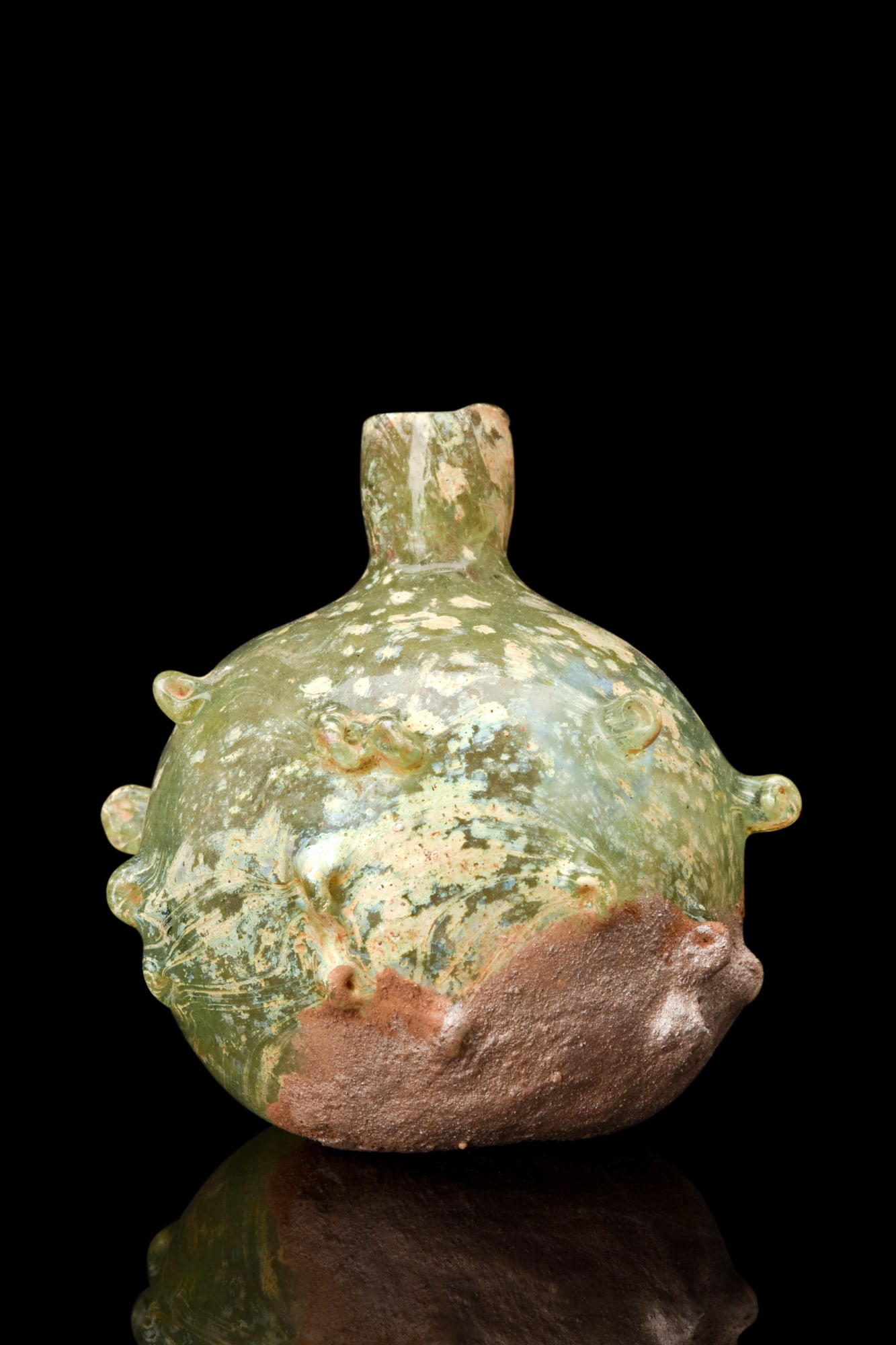 SPIKED ROMAN GLASS FLASK: Ca. 3rd-4th Century AD.A striking Roman glass cup with yellow-green colouring and spotted encrustation. The vessel features a slightly pushed in bottom with a globular body, leading to a narrow neck w