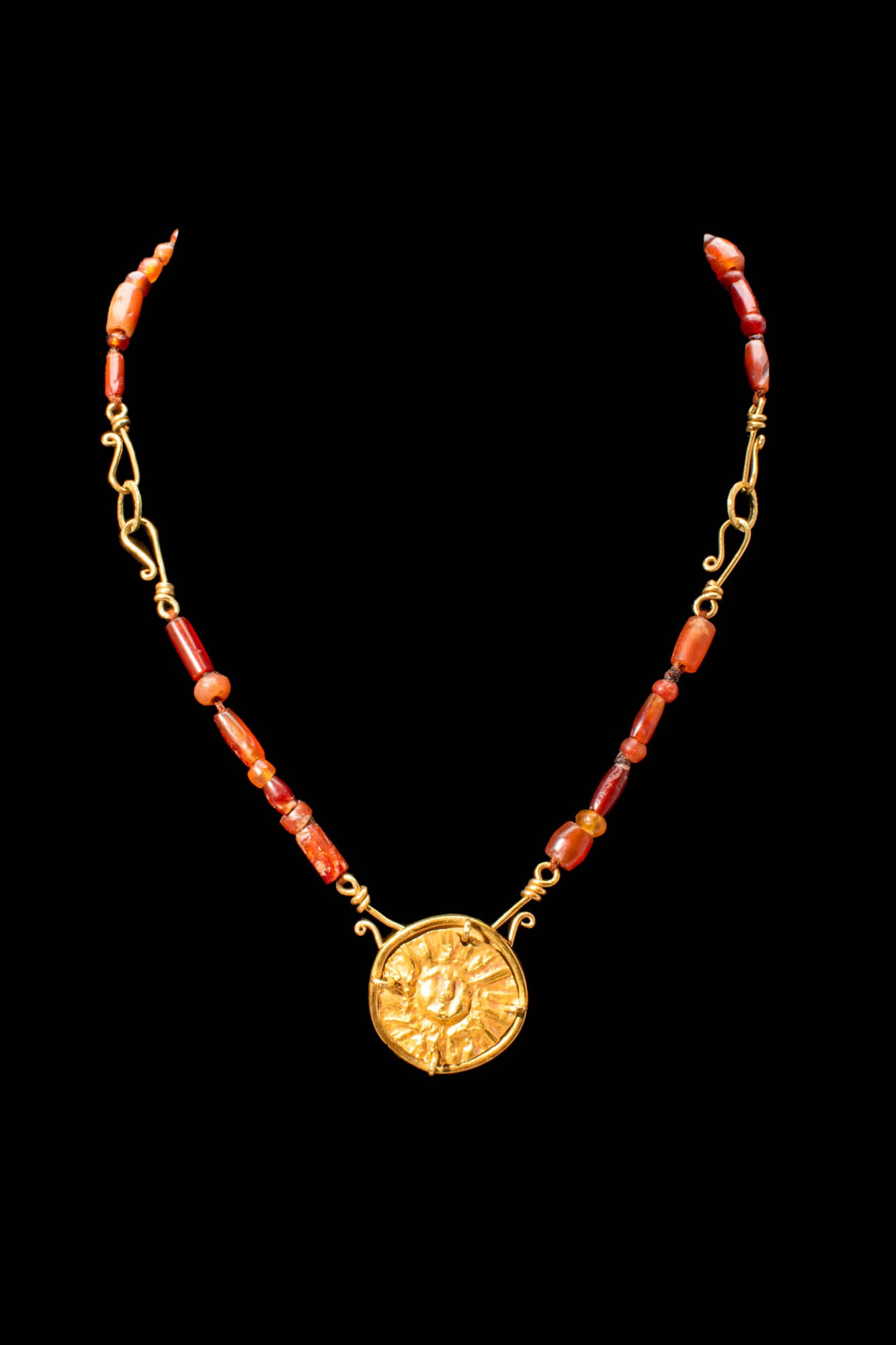 PTOLEMAIC PERIOD CARNELIAN AND GOLD NECKLACE WITH SUN PENDANT: Ptolemaic Period, Ca. 332 - 30 BC. A Ptolemaic period carnelian necklace crafted from dozens of red tube beads alternating with rounded beads. At its centre lies a rare 22 ct gold, sun-shaped pendant 