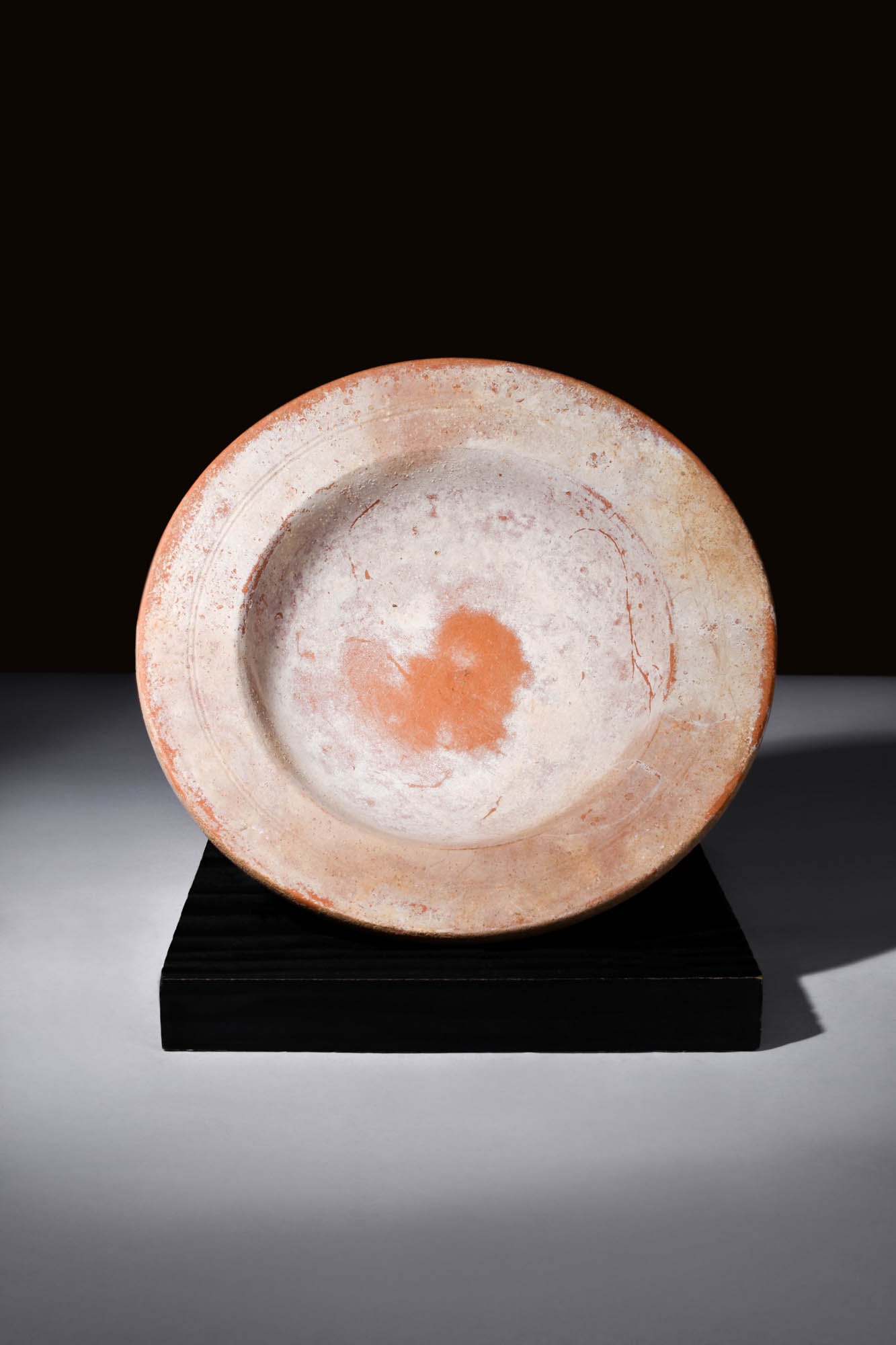 ROMAN REDWARE PLATE: Ca. AD 100 - 300.A redware plate, a confluence of artistry and functionality, commands attention with its rounded basin that gently cradles its form atop a delicate ring foot. The dish, adorned with a