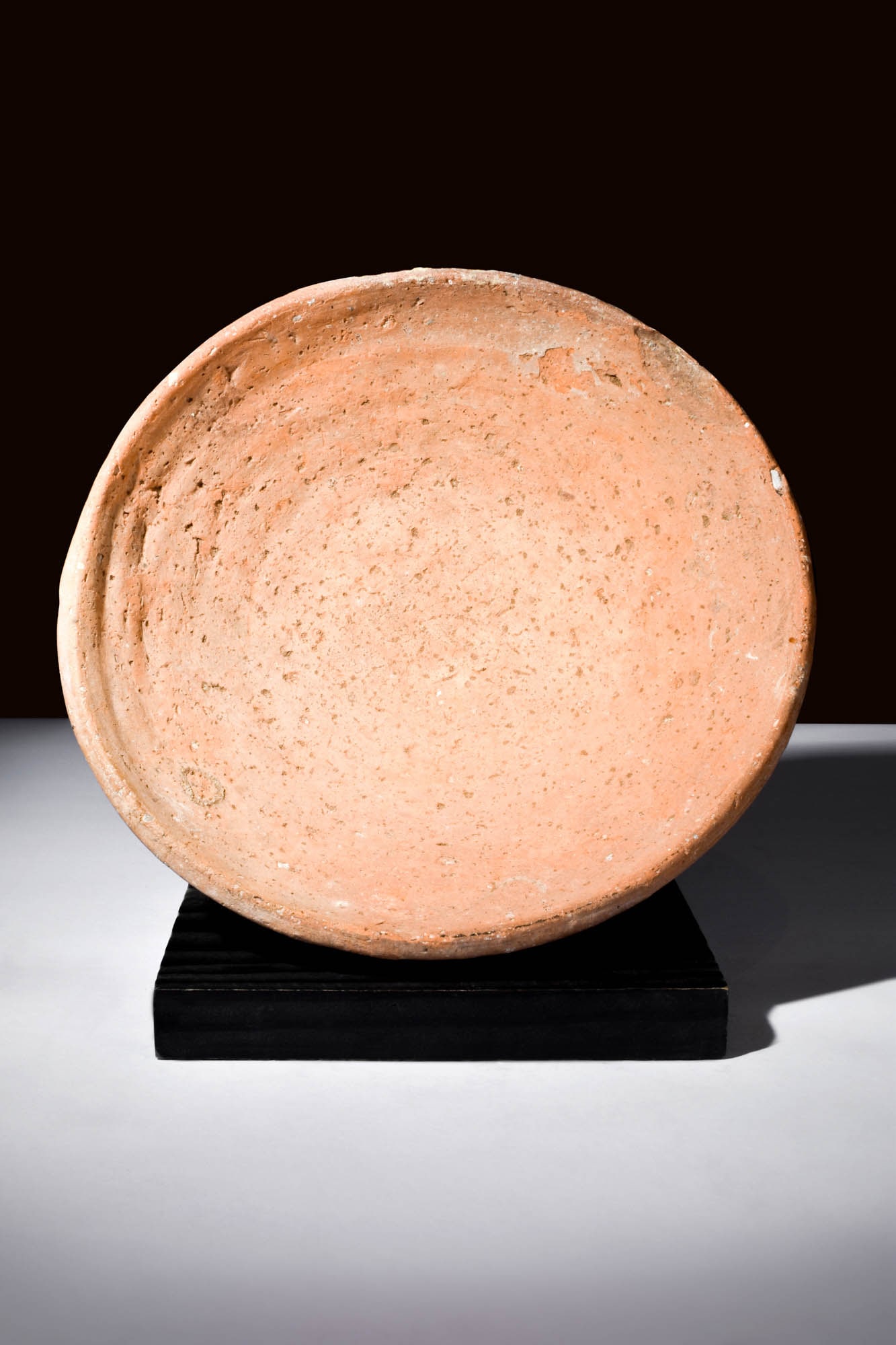 ROMAN REDWARE PLATE: Ca. AD 100 - 300.A redware plate boasts an expansive rounded form, its contours harmoniously transitioning atop a dignified short foot. An air of timeless grandeur pervades the plate's entirety, invit