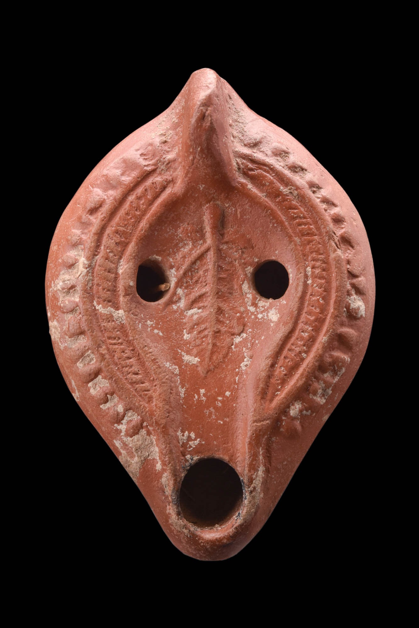 ROMAN NORTH AFRICAN TERRACOTTA OIL LAMP WITH A LEAF: Ca. AD 350 - 450.A redware terracotta oil lamp features a round nozzle and a sculpted lug handle, providing a comfortable grip for the user. The sunken discus at the centre of the lamp is adorned with