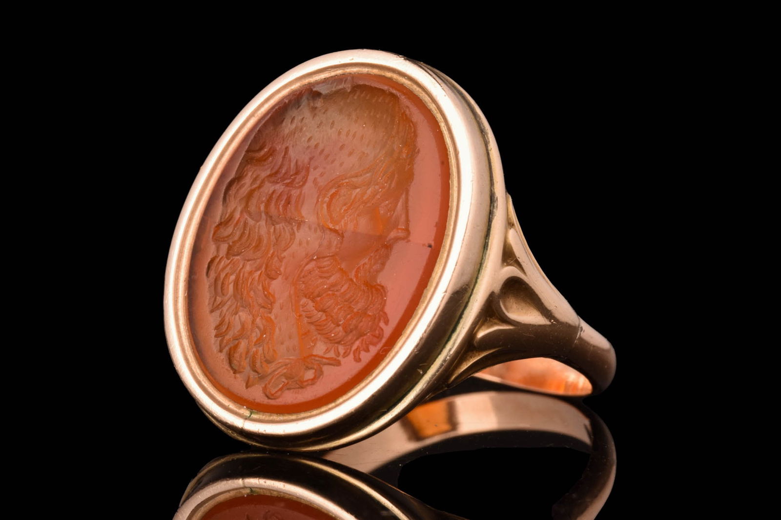 STUNNING NEOCLASSICAL GOLD RING WITH SILENUS INTAGLIO: Ca. AD 1800 - 1900.A gold finger ring composed of a thin hoop with flaring shoulders supporting an oval-shaped frame set with a carnelian intaglio with a right-facing portrait of Silenus. He was a wis