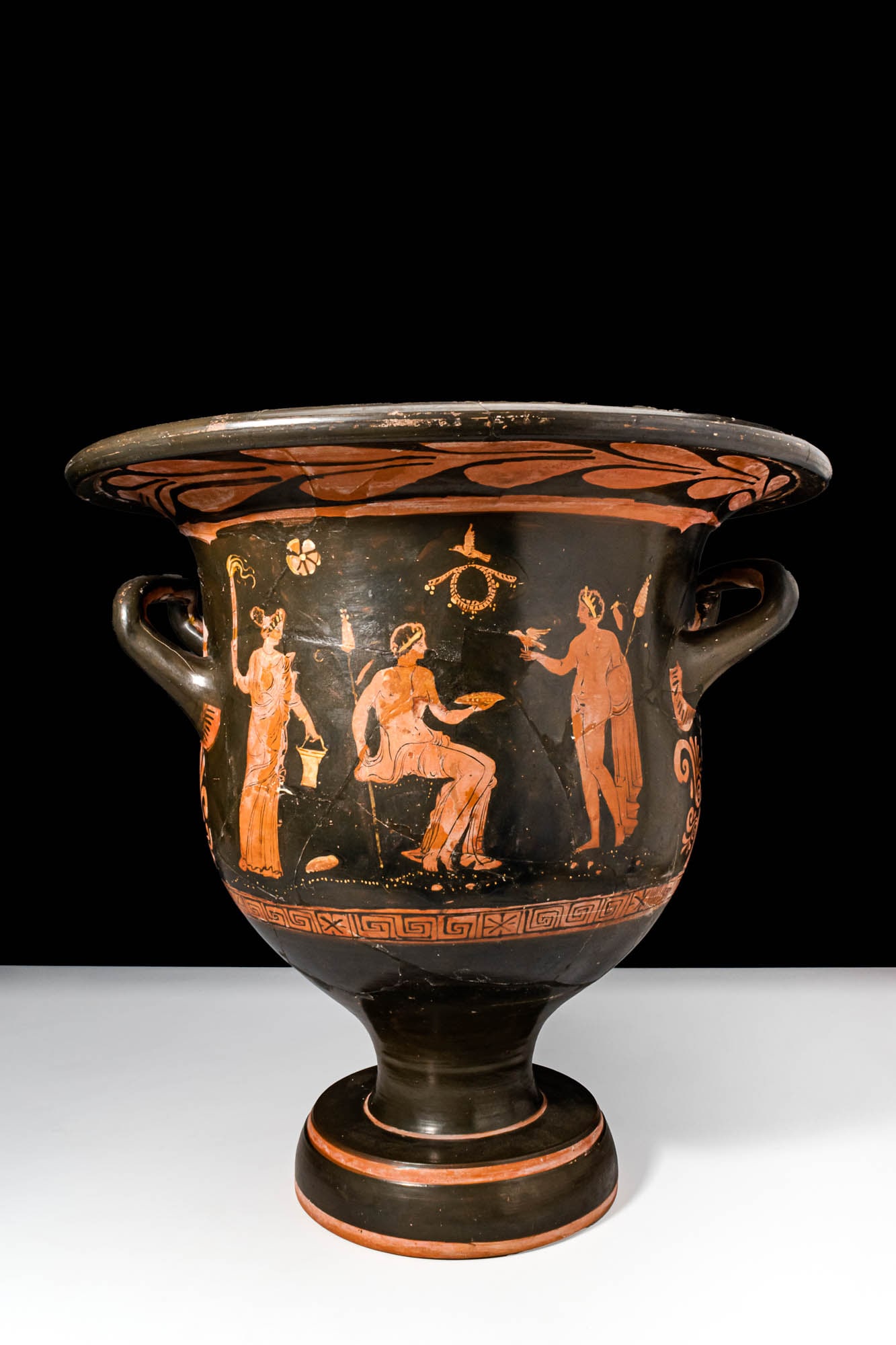 APULIAN BELL KRATER DEPICTING APOLLO: Ca. 400 - 300 BCA red-figure bell krater, a vessel for mixing wine and water during the symposium, crafted from terracotta and decorated with white and yellow details over black glaze. It features a l