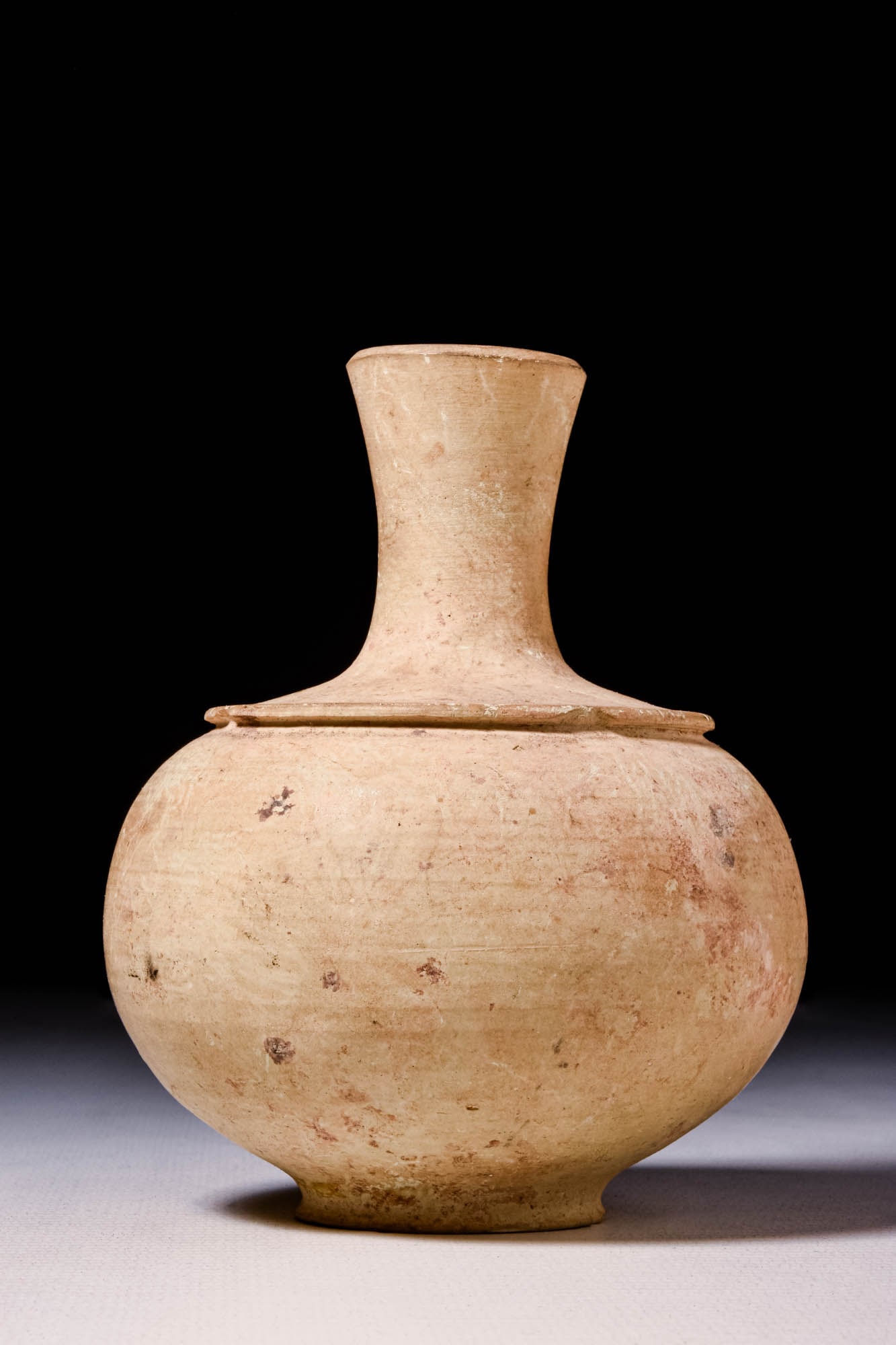 AMLASH POTTERY JAR: Ca. 1200 - 800 BCAn Amlash hand-built redware pottery jar of spherical form with a circular flat base, a narrow neck, and a vertical rim. A circular line protrudes from the shoulders. The vase is pain