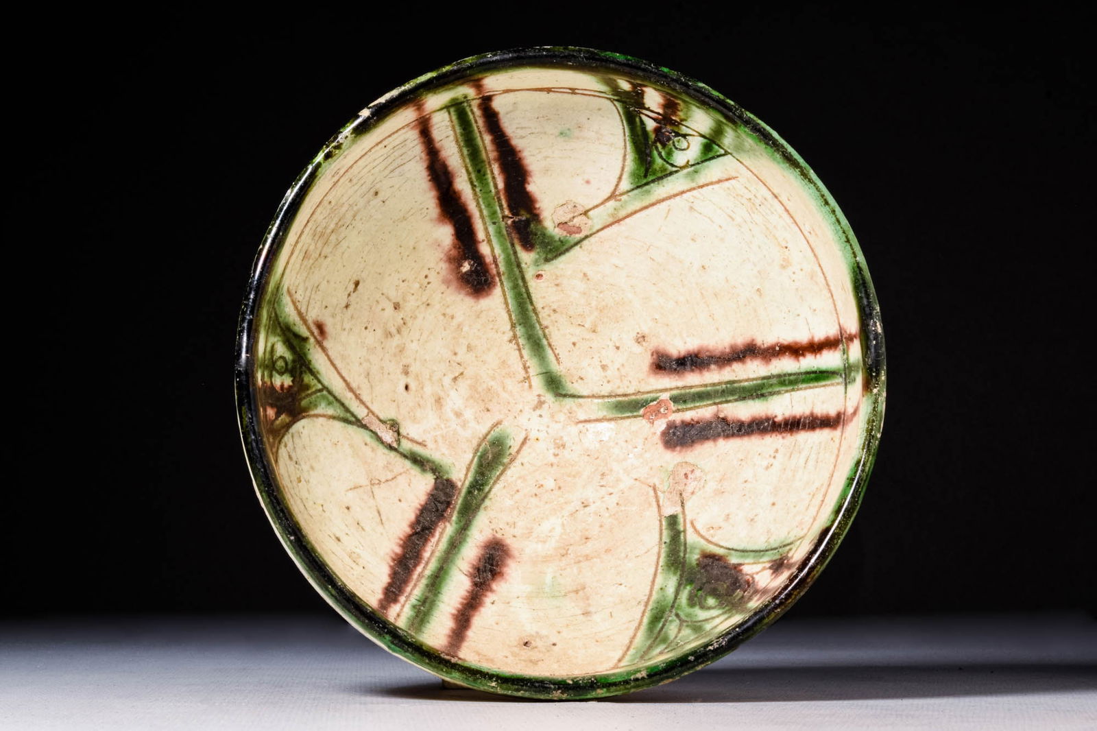 NISHAPUR GLAZED BOWL WITH PHYTOMORPHIC MOTIF: Ca. AD 900 - 1100A Nishapur glazed pottery bowl sitting upon an unglazed discoid foot with a deep basin, all enveloped in creamy white and emerald green glaze. The exterior of the straight walls are a