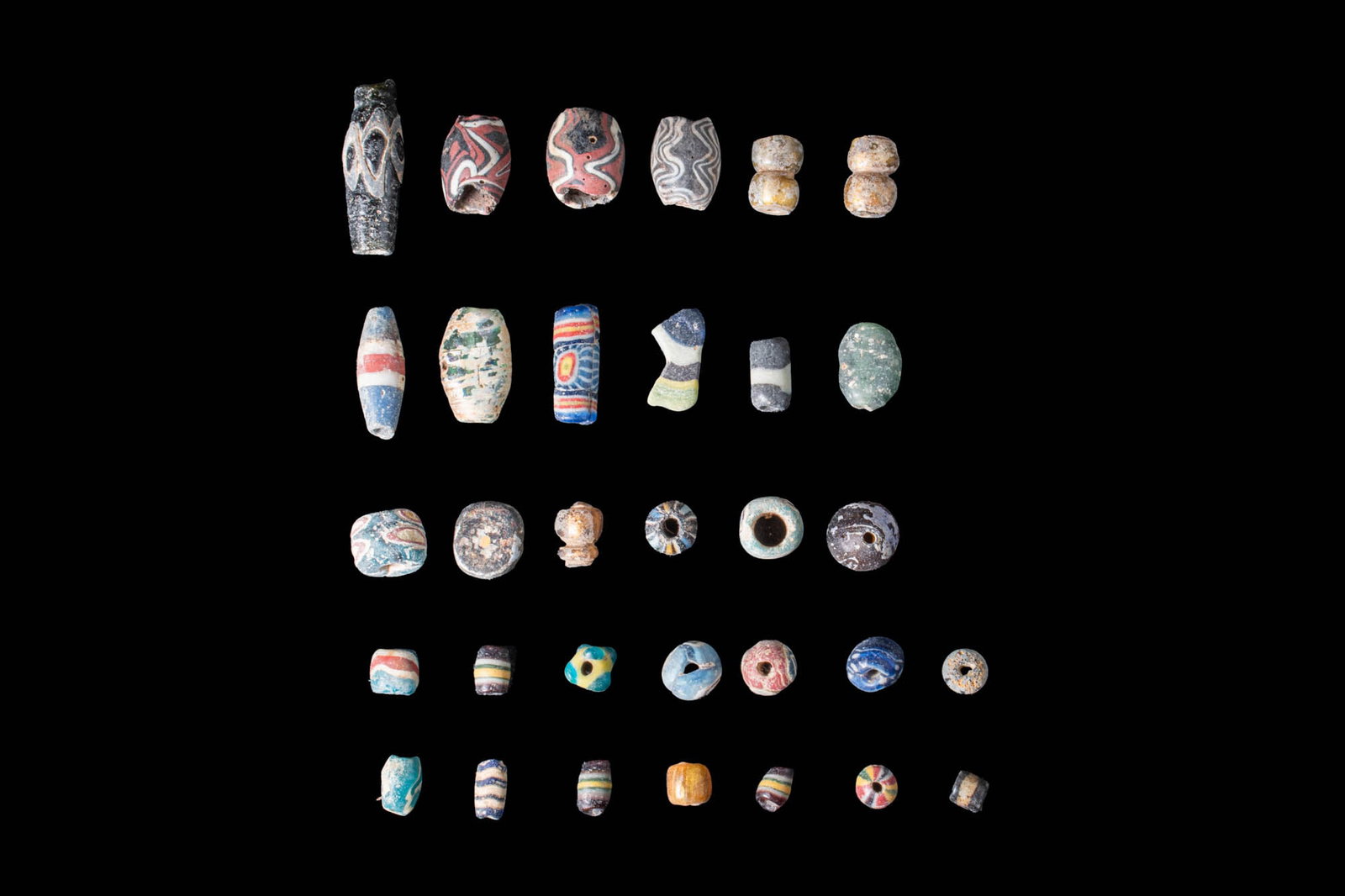 LARGE COLLECTION OF PHOENICIAN MOSAIC GLASS BEADS: Ca. 600 - 300 BC. A fabulous collection of thirty two Phoenician beads. The elegant ensemble boasts an impressive variety of vibrant hues, fascinating forms and mesmerising designs. Size: 5-18mm x 5-1