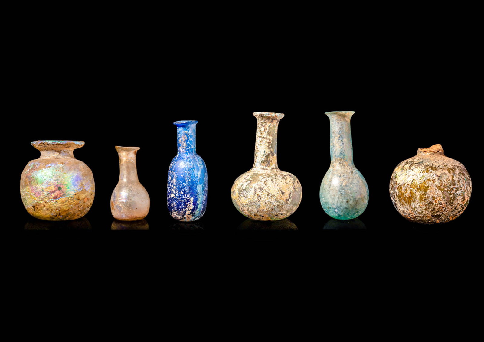 COLLECTION OF ROMAN GLASS UNGUENTARIA: Ca. AD 100 - 300. A collection of small Roman glass unguentaria, with differing shapes and colours. These unguentaria have layers of rainbow-hued iridescence. They are formed by the flared, vertical r