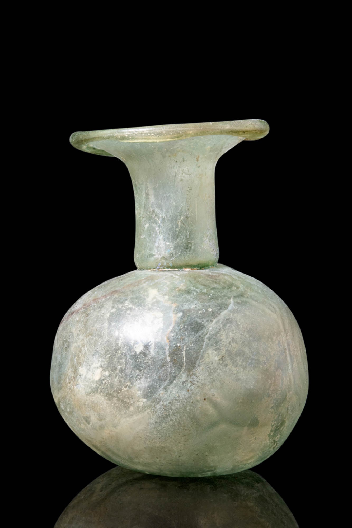 LARGE ROMAN PALE GREEN GLASS UNGUENTARIUM: Ca. AD 100 - 300. A Roman pale green glass unguentarium with a circular concave base and a globular body. The body tapers into a short, wide neck with a folded, flared rim. A beautiful silvery iridesc