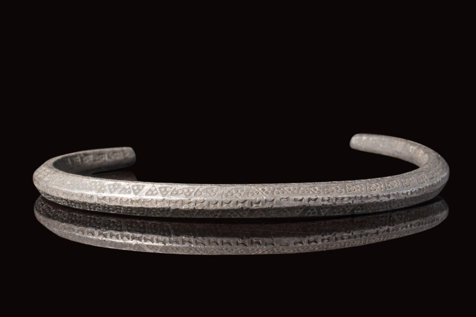 VIKING SILVER BRACELET WITH STAMPED TRIANGLES: Ca. AD 900 - 1100.A stunning bracelet with mid rib. It exhibits a lustrous surface, curved body, and small tapering finials. The body is adorned with hundreds of stamped triangles. For similar see: Th