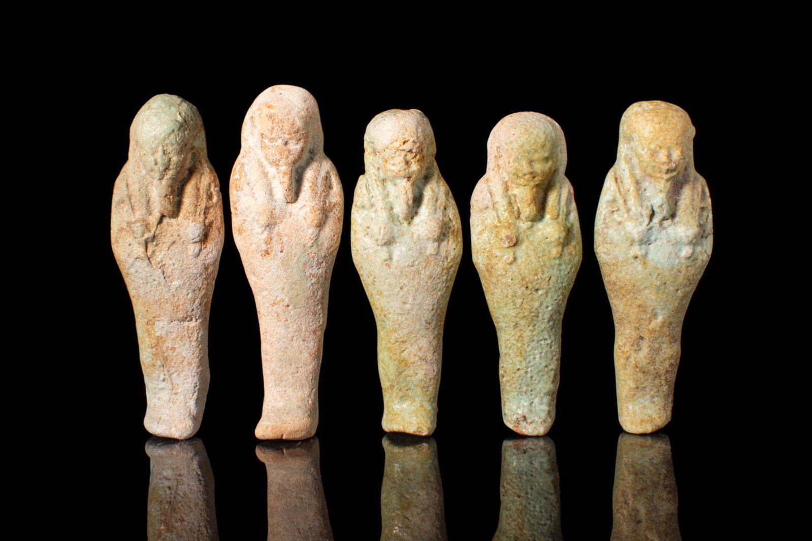 COLLECTION OF EGYPTIAN PALE GREEN USHABTIS: Late Period, Ca. 664 - 30 BC.A collection of five faience ushabtis covered in layers of reflective pale green-hued glaze. The figures stand in mummiform with fused legs and feet; a long Nemes surround