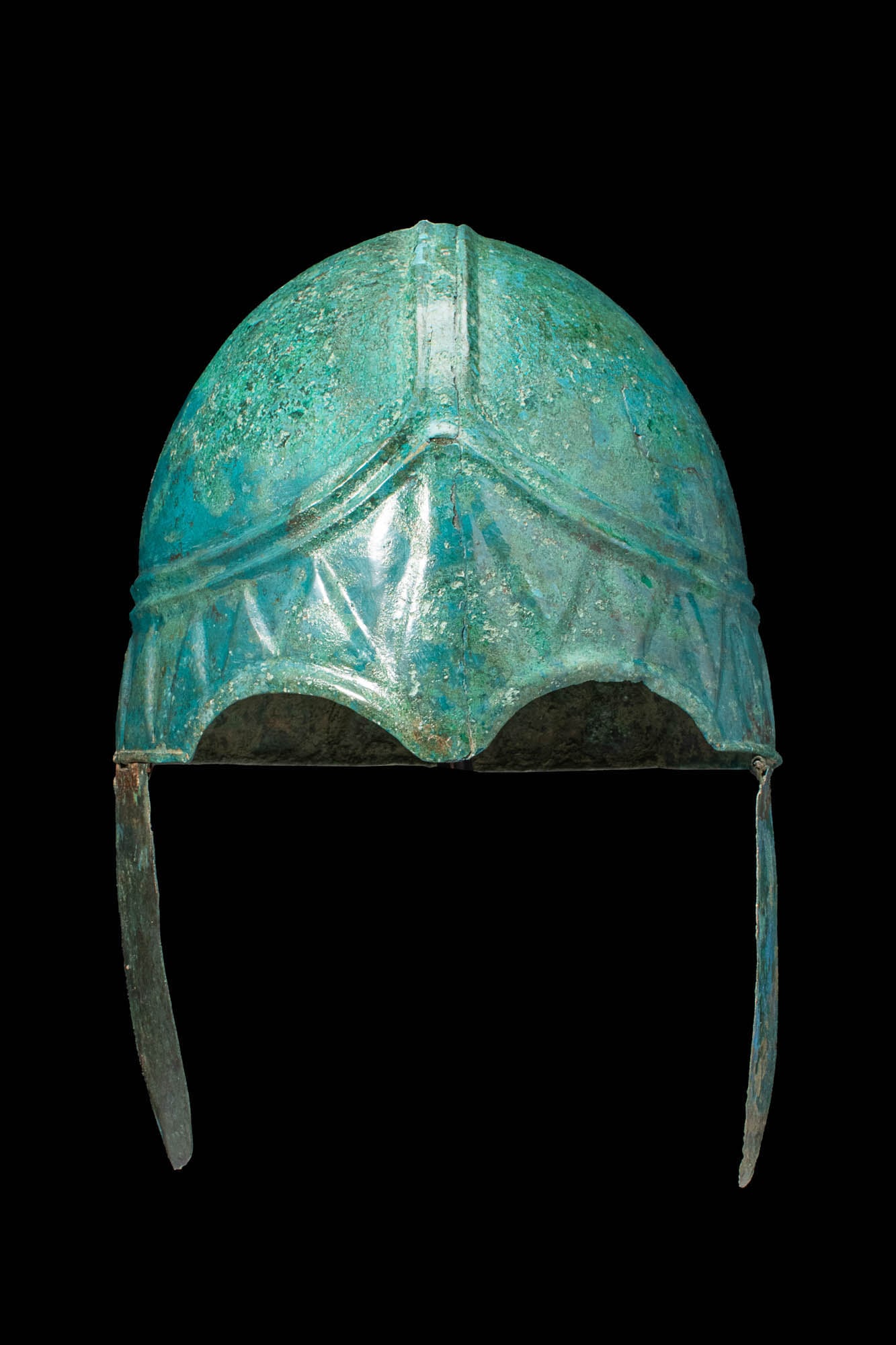 STUNNING CHALCIDIAN BRONZE HELMET: Ca. 500 BC.A striking Chalcidian bronze helmet with two curved cheek pieces attached with iron pins that form a hinge.The forehead has two sweeping central ridges and an overhanging brow line embellis
