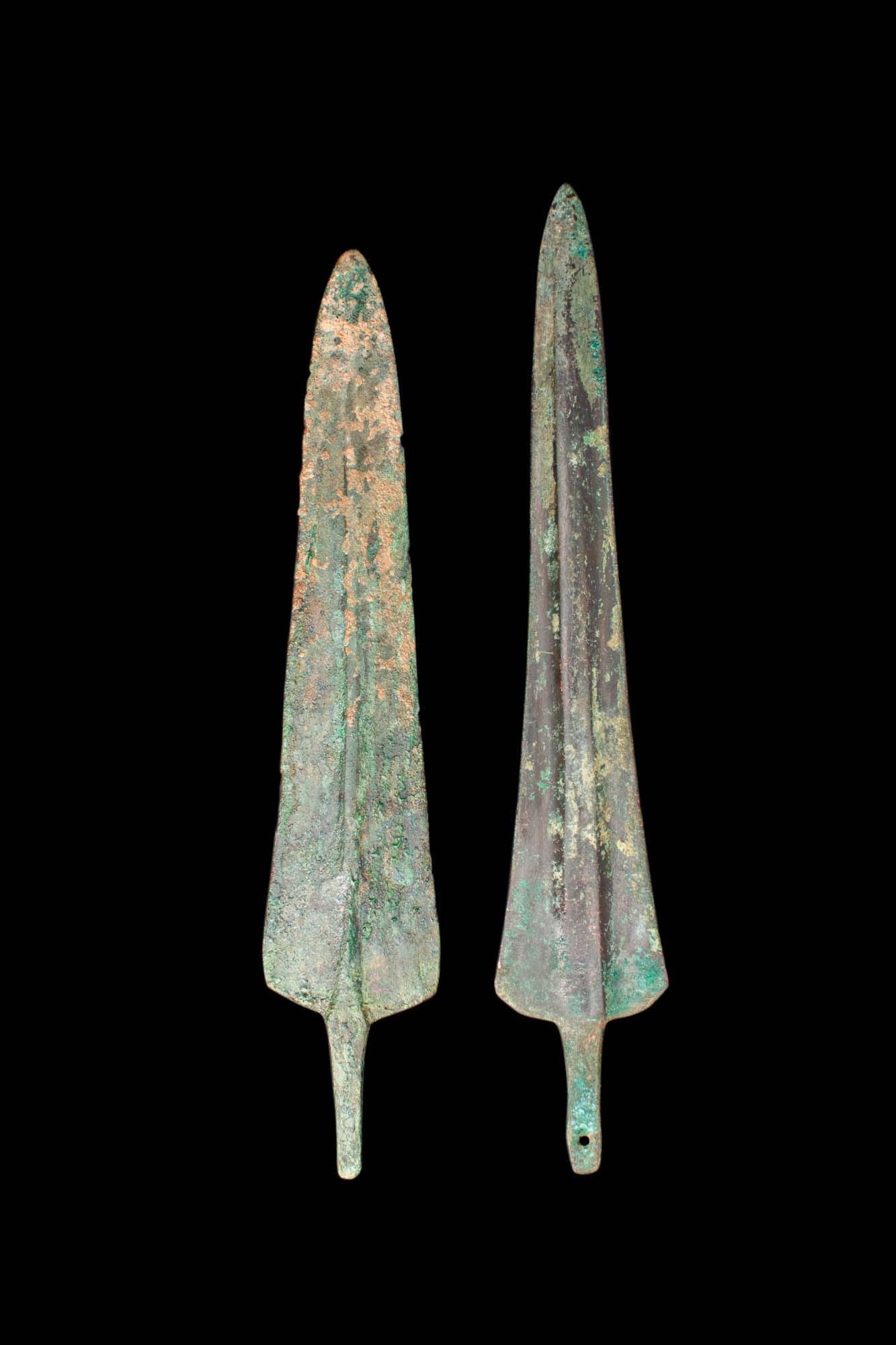 PAIR OF EARLY GREEK / WESTERN ASIATIC DAGGERS: Ca. 1200 - 800 BC.A pair of cast bronze daggers. The weapons have dual, tapered edges leading to a pointed tip, with a shallow midrib that ends in a short tang. For similar see: Christie's, Live Aucti