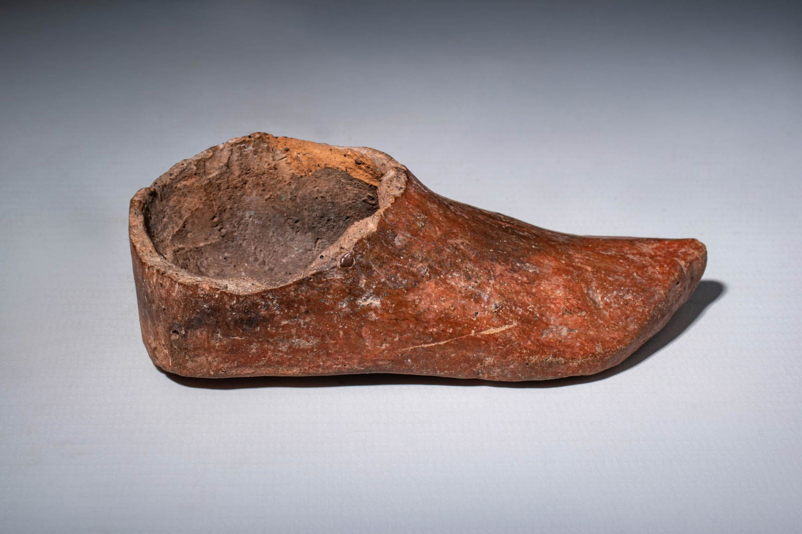 ISLAMIC POTTERY SHOE: Ca. AD 700. A hollow pottery model of a shoe made from red clay. It features a flat sole and a slightly pointed toe box. Size: 110mm x 45mm; Weight: 95g. Provenance: Prince collection, 1990s-2014; Ex.