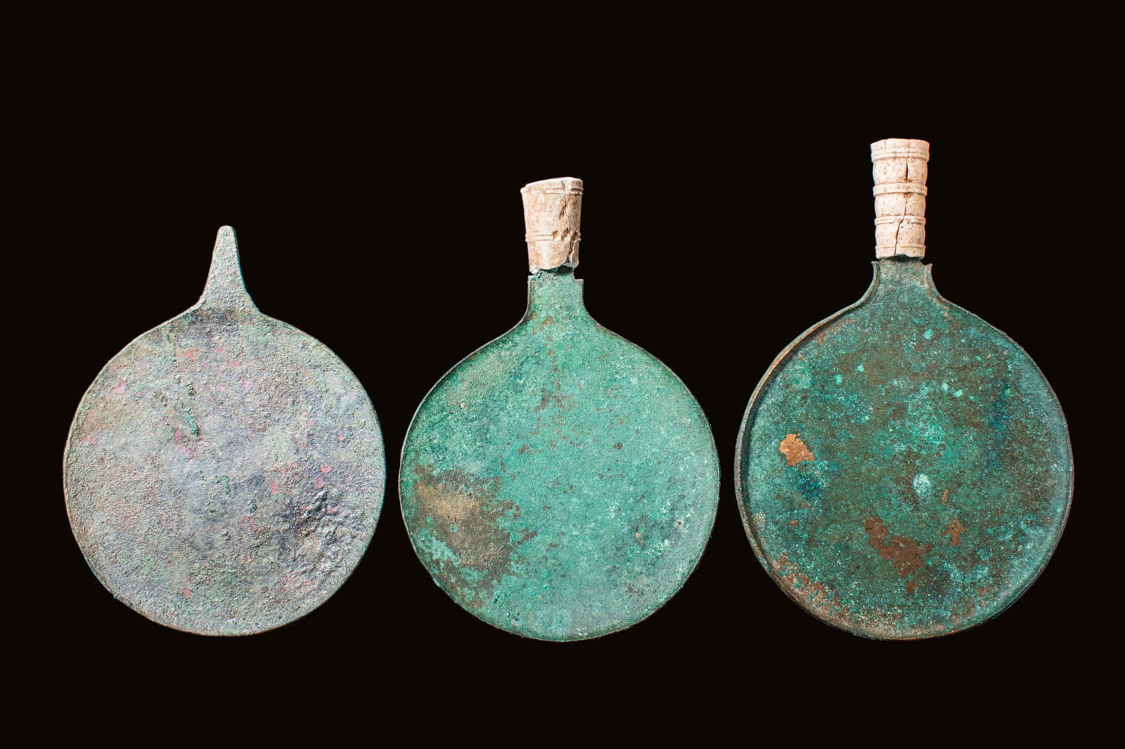 COLLECTION OF ETRUSCAN BRONZE MIRRORS WITH BONE HANDLES: Ca. 400 BC. A collection of three bronze mirrors. The round discs have a slightly concave body with a short rim and a small tang. The bone handle is decorated with encircling lines and concentric patt