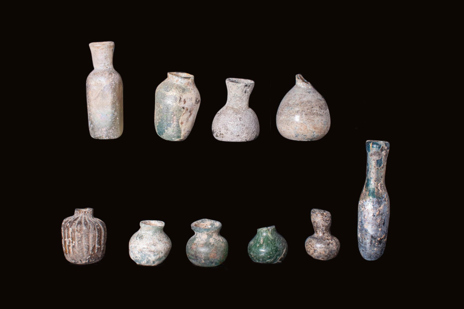 GROUP OF ROMAN GLASS VESSELS: Ca. AD 1 - 400.A group comprising 10 glass containers, displaying various shapes and styles. Among them are bulbous flasks, bottles and jars, each exhibiting exquisite craftsmanship and design typical