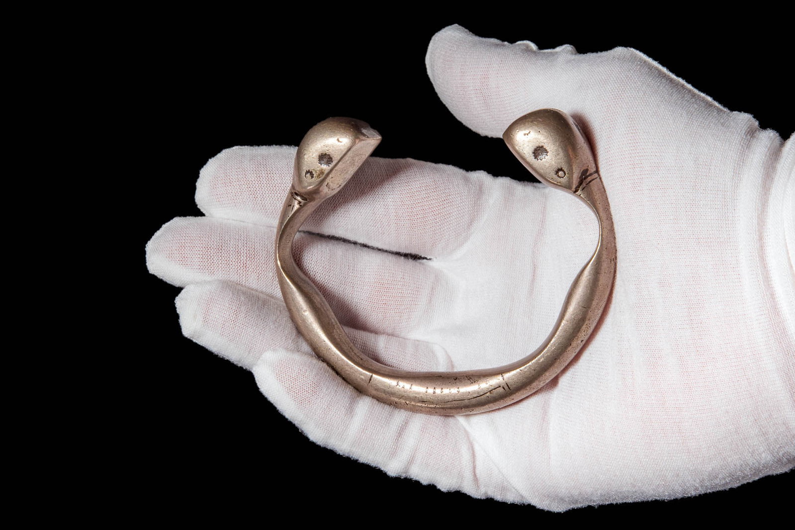 OLD TUAREG SILVER BRACELET WITH SNAKE FINIALS: Ca. AD 1800. A silver bracelet with a thick, rounded band that curves into an open-ended form. The terminals are prominent, each with a slightly flattened top and small circular indentations resemblin
