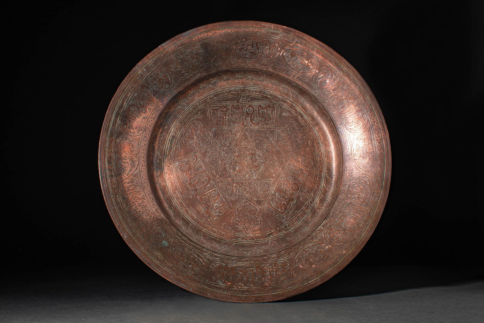 A MAMLUK REVIVAL COPPER ALLOY CHARGER: Egypt or Syria, Ca. 19th century AD. A copper charger of circular form with a flat base and flaring rim, adorned with a fine calligraphic section, possibly a blessing or benedictory text, featuring a