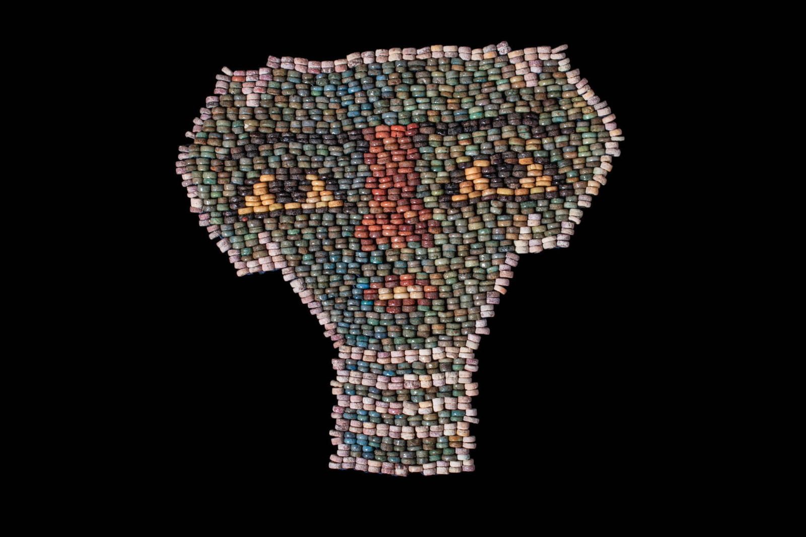 EGYPTIAN FAIENCE BEADED MUMMY MASK: Late Period, ca. 663-323 BC. A mummy mask restrung of delicate faience beads in green, cream, red, and black. The face is highly stylised with large trapezoidal eyes, long, thin brows, a broad, undeta