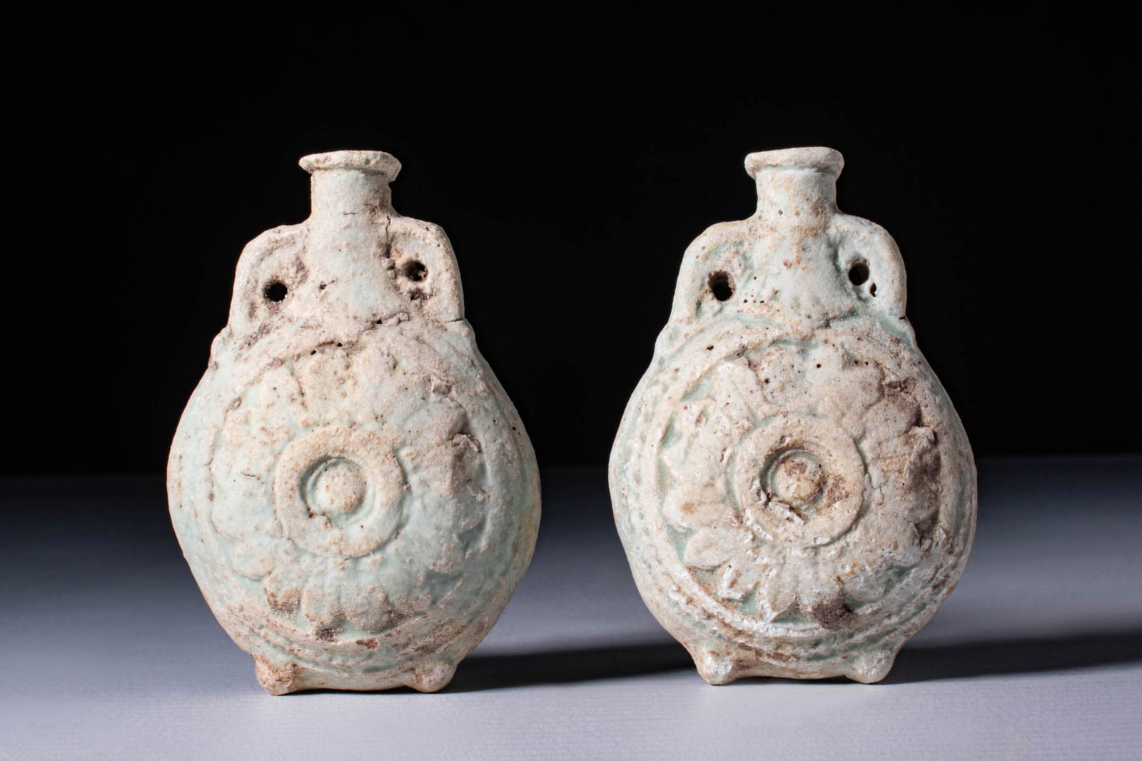 PAIR OF ROMANO-EGYPTIAN FAIENCE FLASKS DEPICTING ANUBIS: Ca. 30 BC - AD 200. A pair of turquoise-glazed faience flasks, each with a rounded and flattened body, and a short, cylindrical neck flanked by small arched handles. One side of each bottle is moulded