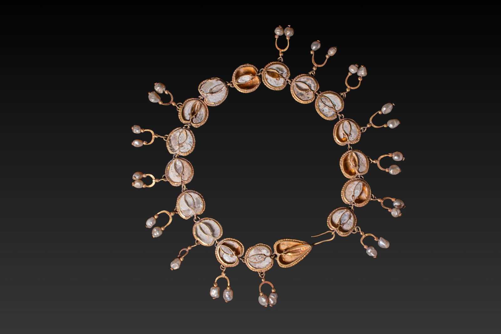 ROMAN HIGH KARAT GOLD AND PEARLS NECKLACE: Ca. AD 100 - 250. A necklace formed of a series of 17 gold settings containing inset white glass elements with central ridges, framed by beaded wire. Between each pair of settings are short linking lo