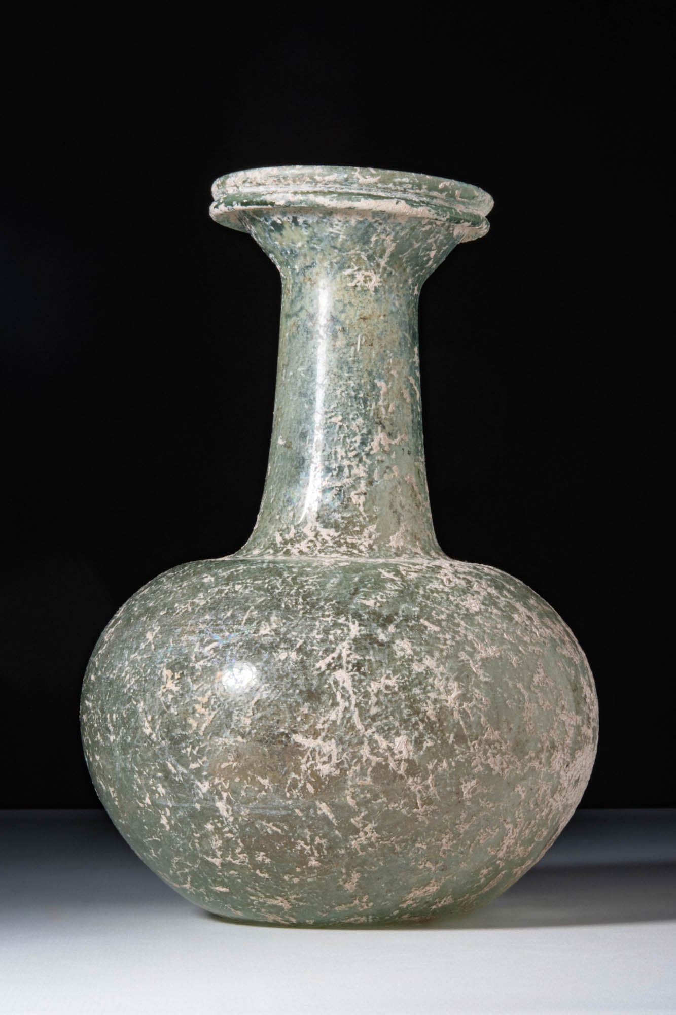 HUGE ROMAN GLASS APPLE-SHAPED UNGUENTARIUM: Ca. AD 1 - 200. A translucent greenish glass unguentarium with an apple-shaped body and a slightly concave base. The tall cylindrical neck terminates in a broad, flared rim folded outwards.For similar