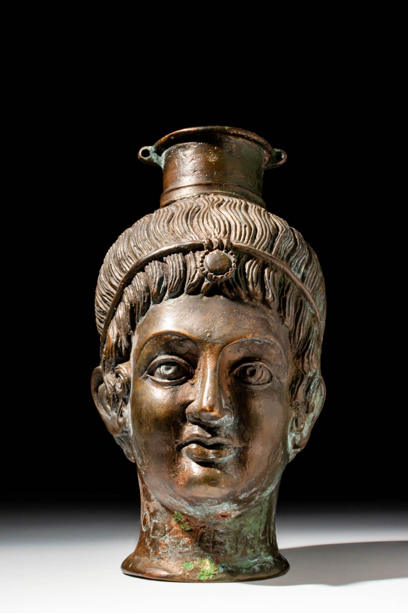 NEOCLASSICAL BRONZE HEAD-SHAPED OINOCHOE WITH SCRIPT: CA. 1900 AD OR EARLIER . A bronze flask in the form of a youthful male head. The vessel is cast with finely modelled facial features, almond-shaped eyes with defined lids, full lips, and a rounded chi