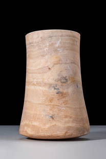 LARGE BACTRIAN ALABASTER BEAKER: Ca. 2000 - 1000 BC. A cylindrical alabaster vessel with thick walls and a tall body that flares towards the rounded base. The surface displays natural banding in beige and light brown hues.For similar