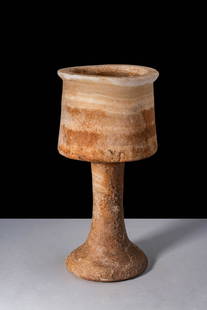BACTRIAN ALABASTER CHALICE: Ca. 2200 - 1800 BC. A tall alabaster vessel with a wide cylindrical cup with a gently everted rim, rising from a long, slender stem that flares into a broad, circular base. The stone exhibits layered