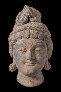 GANDHARAN STONE HEAD OF BUDDHA: Ca. AD 3-4th century or later. A detailed head of Buddha. The youthful face is modelled with gentle features, almond-shaped eyes cast downward in a serene expression, full lips forming a faint smile,