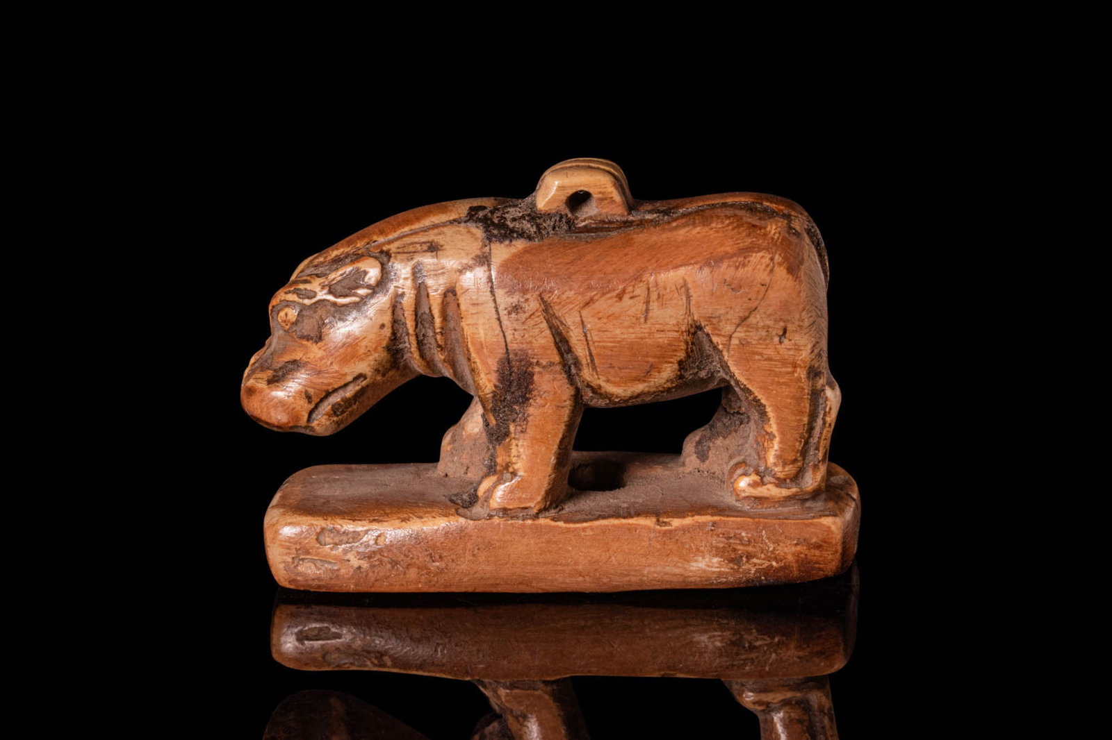 EGYPTIAN BONE FIGURINE OF HIPPOPOTAMUS: Late period, Ca. 664 - 332 BC. A carved bone figurine representing a hippopotamus with lowered head and incised detailing along the body and limbs. The figure stands on an integral rectangular base pi