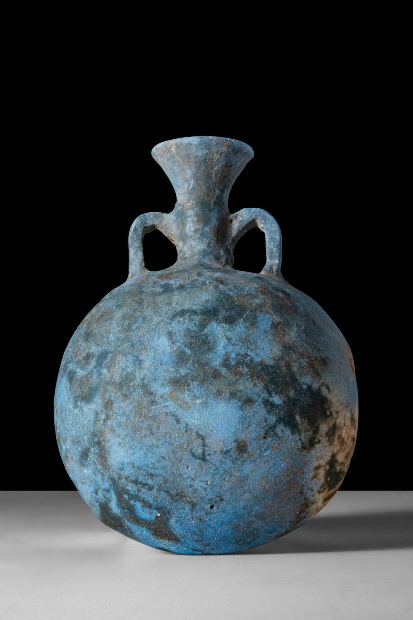 EGYPTIAN BLUE PILGRIM FLASK: New Kingdom, Ca. 1550 - 1069 BC. An Egyptian blue flask with a flattened circular body, cylindrical neck, and wide, flaring mouth. Twin loop handles rise from the shoulders to the neck.Size: 80mm x 65