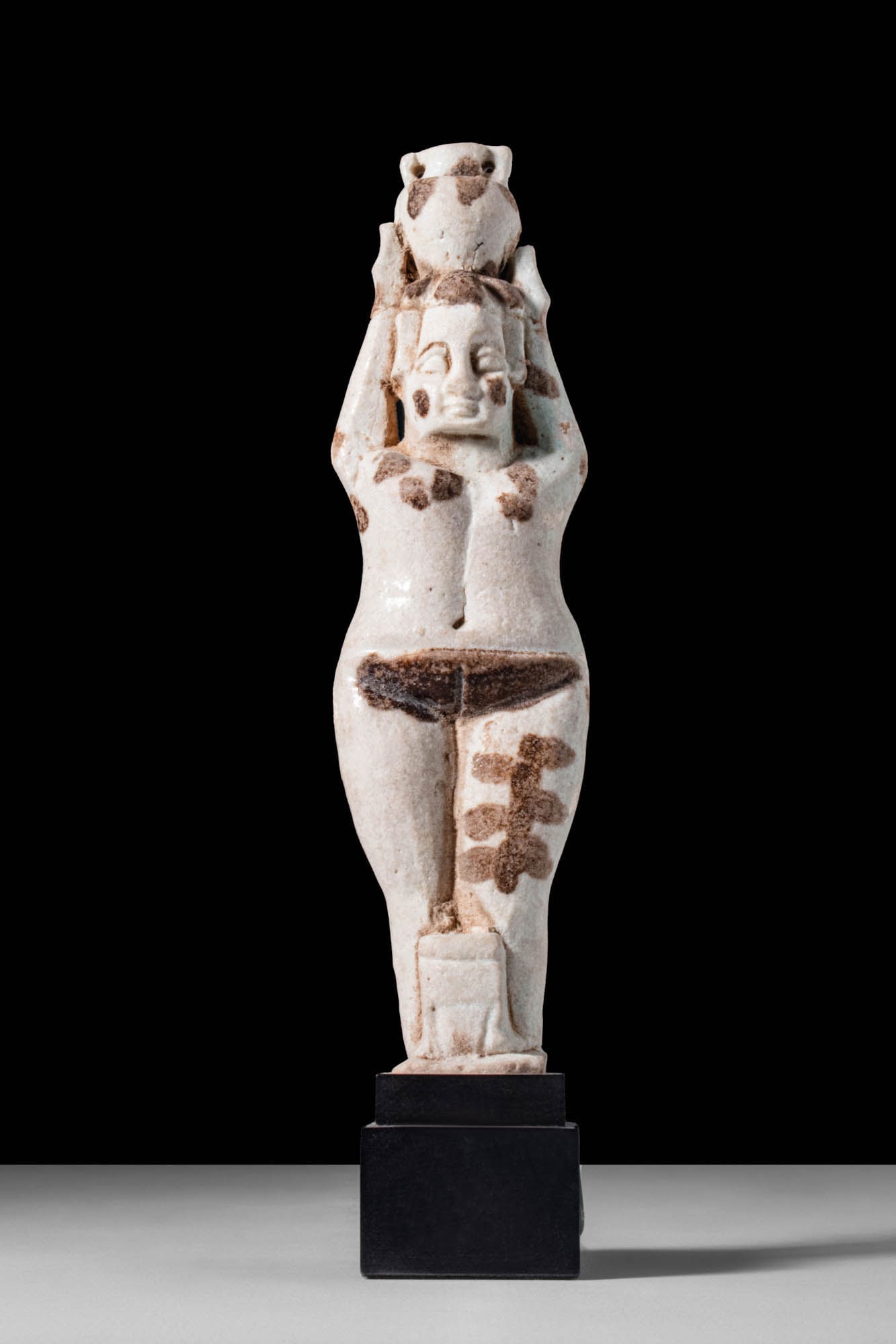EGYPTIAN FAIENCE FIGURE OF NUDE FEMALE FIGURE HOLDING A VASE ON HER HEAD: Third Intermediate Period, 22nd-23rd Dynasties, Ca. 945 - 715 BC. A faience figure depicting a nude female standing upright, with both hands supporting a two-handled amphora balanced on her head. Her