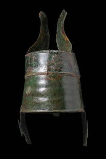 RARE URARTIAN BRONZE CEREMONIAL HELMET: Ca. 800 - 700 BC. A bronze helmet formed of two joined horizontal bands creating a cylindrical body, with a pair of curved cheek pieces riveted to the lower rim. The upper edge is fitted with a tall,