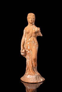 HELLENISTIC TERRACOTTA STATUETTE OF A WOMAN: Ca. 300 - 200 BC. A terracotta statuette depicting a standing female figure clad in a finely draped chiton. The folds are modelled in soft, flowing lines that accentuate the contours of the body. Her