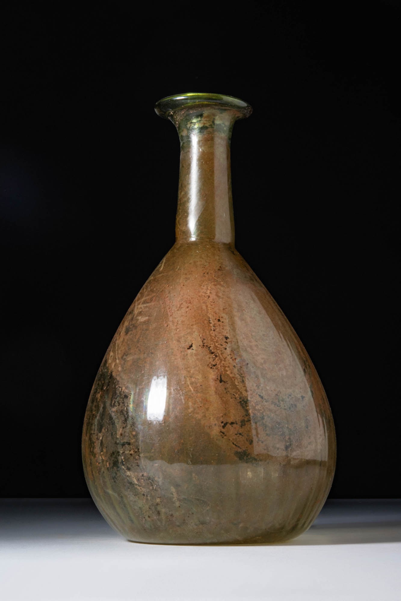 LARGE GALLO-ROMAN PEAR-SHAPED UNGUENTARIUM: Ca. AD 1 - 200. A translucent greenish glass unguentarium. Its pear-shaped body tapers towards a concave base and continues into a tall cylindrical neck with a flared, outward-folded rim.For similar s