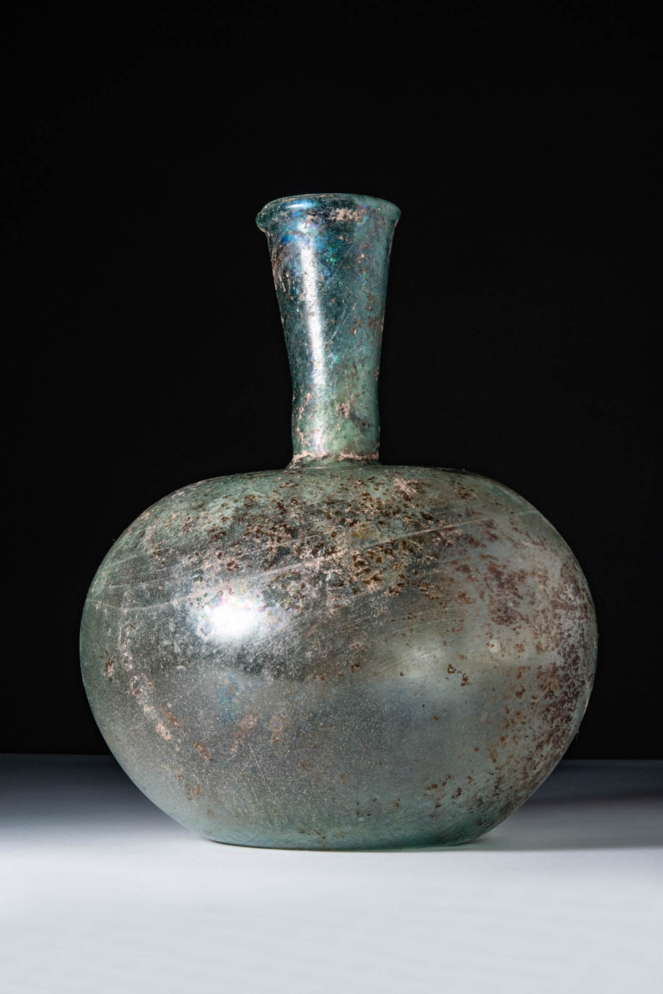 HUGE ROMAN GLASS APPLE-SHAPED UNGUENTARIUM: Ca. AD 100 - 200. A translucent pale green glass unguentarium with a broad, apple-shaped body and a long cylindrical neck that expands into a wide, flaring rim with a rounded lip. For similar see: Lig