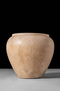 EGYPTIAN ALABASTER VOTIVE VESSEL: Old Kingdom, Ca. 2900 - 2200 BC. An alabaster vessel rising from a flat base, with a broad rounded shoulder leading to a short, narrow rim. The surface is smooth, displaying a pale beige tone with sub