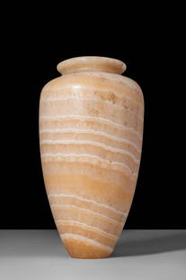 EGYPTIAN ALABASTER PYRIFORM VOTIVE VESSEL: Old Kingdom, Ca. 2900 - 2200 BC. A pyriform vessel carved from banded alabaster. The body tapers to a flat base and swells outward before narrowing slightly towards the short neck, which is topped by