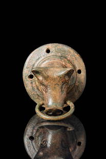 ROMAN BRONZE DOOR APPLIQUÉ IN THE FORM OF A BULL'S HEAD: Ca. AD 1 - 300. A cast bronze mount in the form of a bull’s head, with prominent ears, narrow eyes, and a pronounced snout with well-defined nostrils. The head is attached to a large circular flange